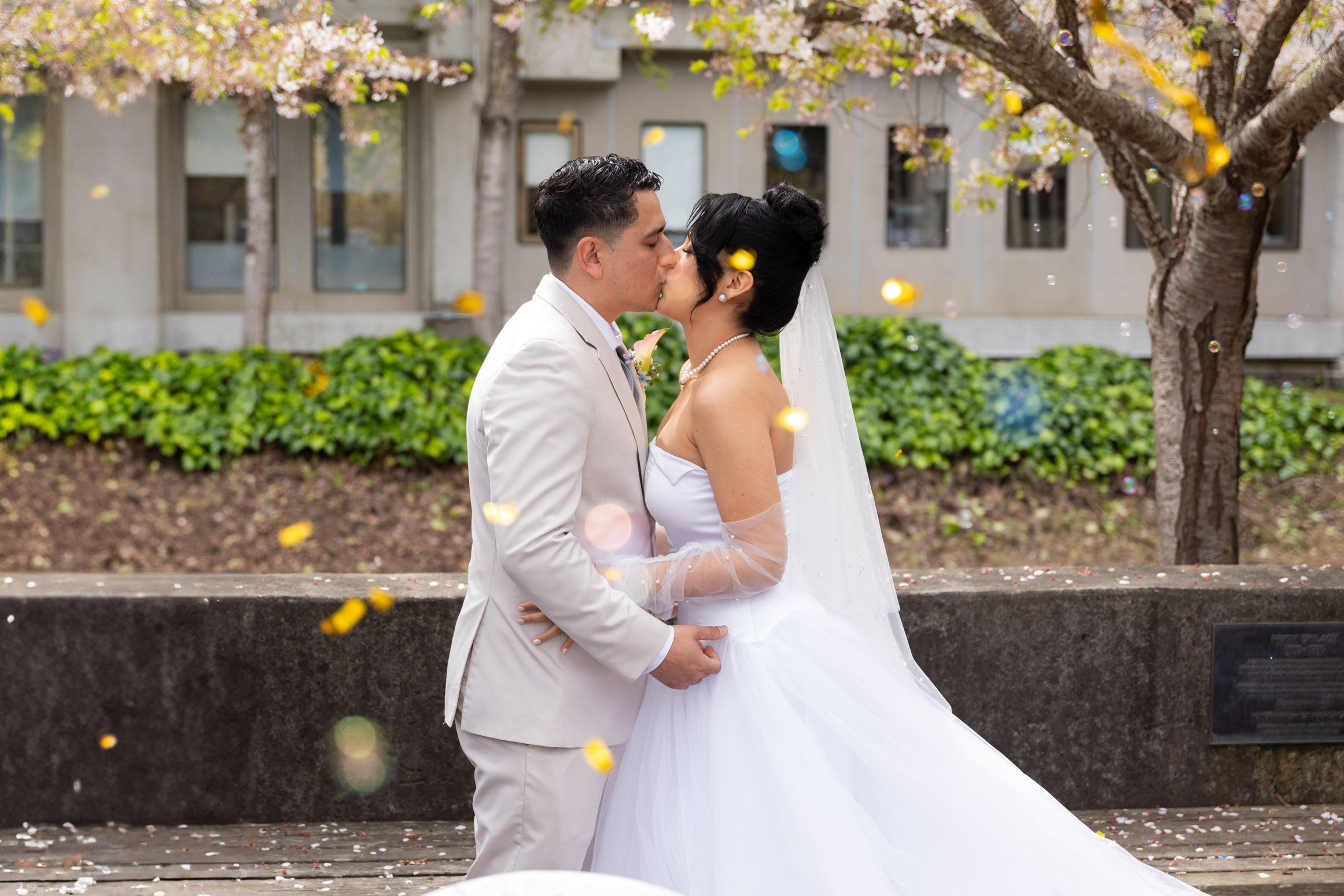 A tender moment shared between a couple in wedding attire beneath a blooming tree with falling yellow leaves.