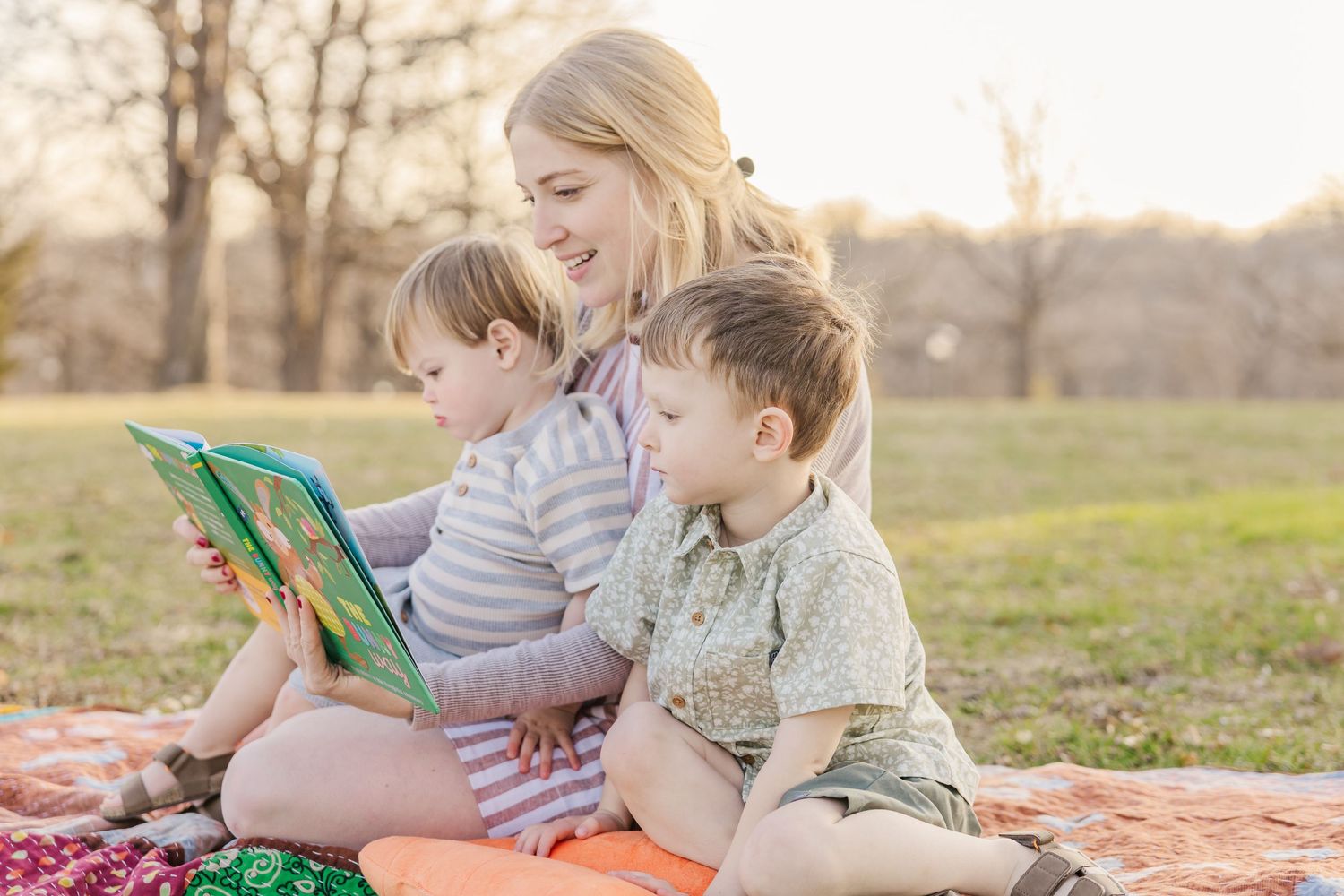 Reading together on an orange blanket outdoors during a peaceful sunset in a grassy field.
