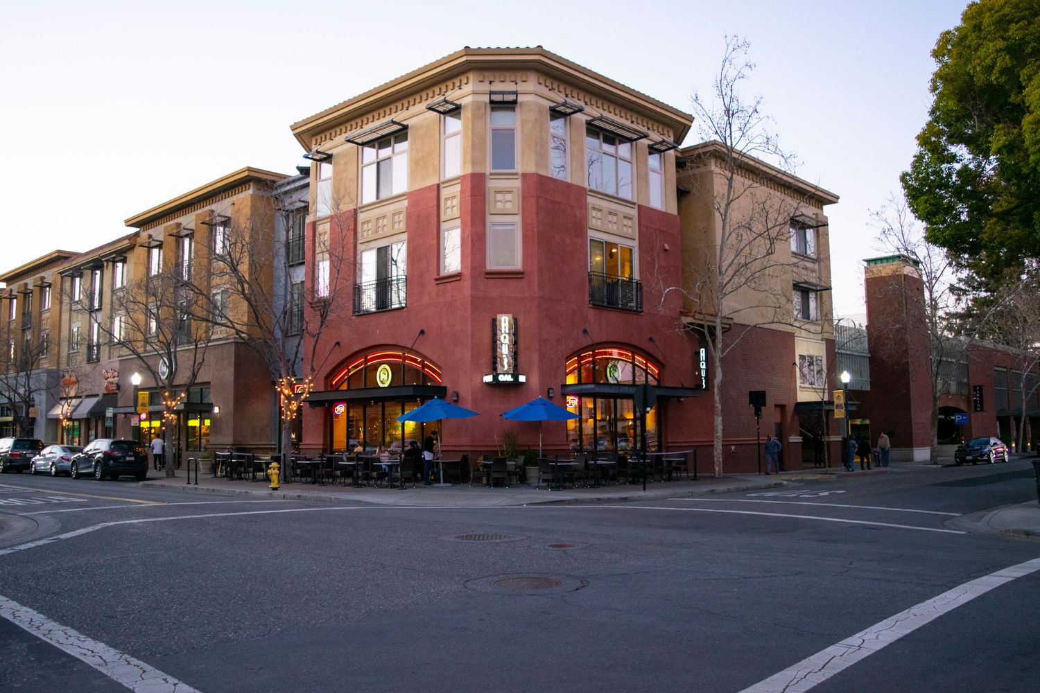 Modern brick apartment building with retail space on the corner of an urban street at dusk.