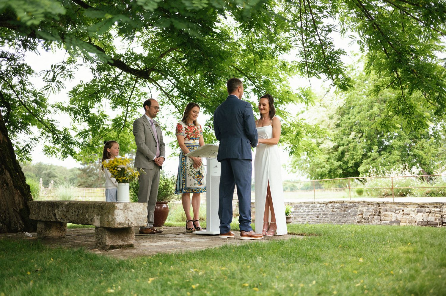 Cérémonie laïque en extérieur sous un arbre, avec un couple échangeant ses vœux entouré de proches.