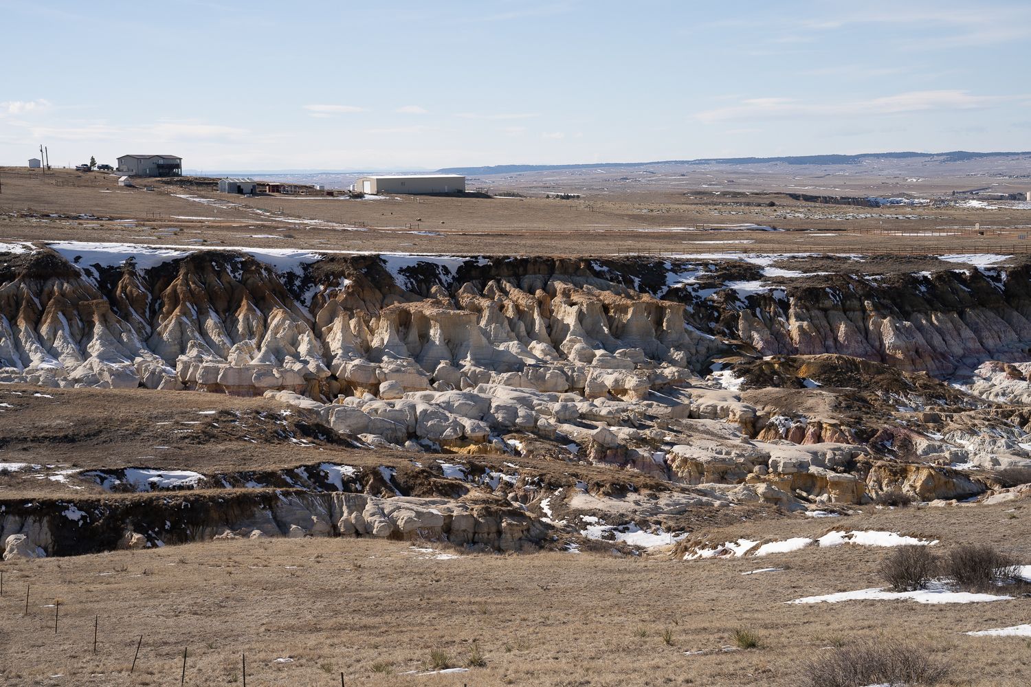 Eroded rock formations and cliffs create dramatic layered landscape in barren winter terrain with patches of snow.