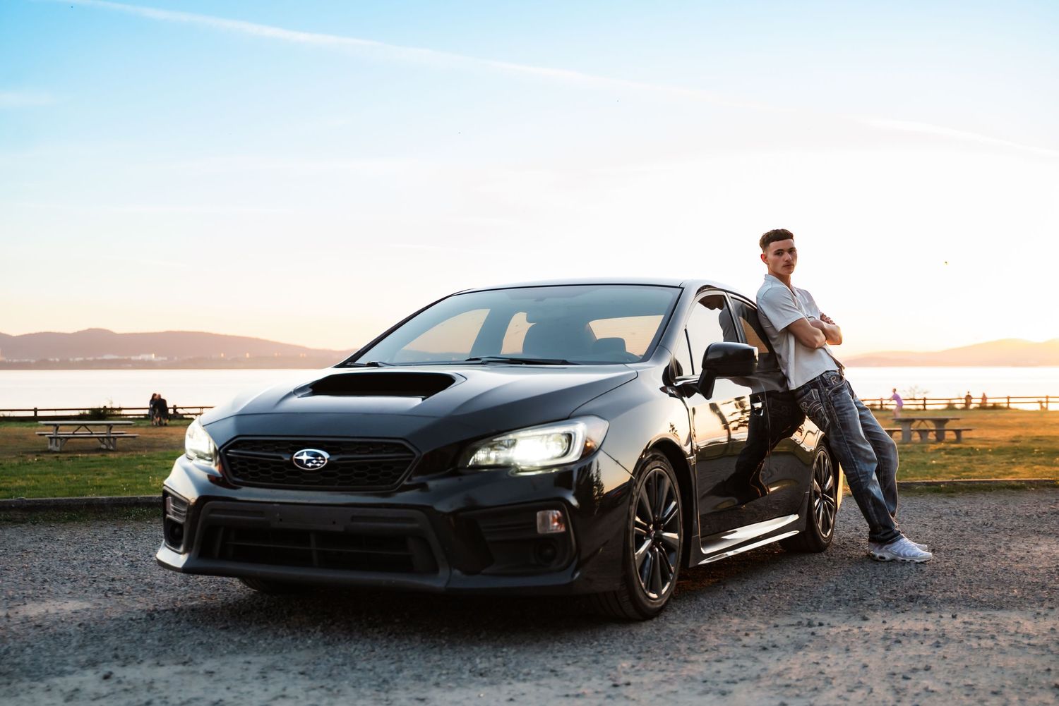 teen guy leans on his car backed by the sunset at Bayview State Park