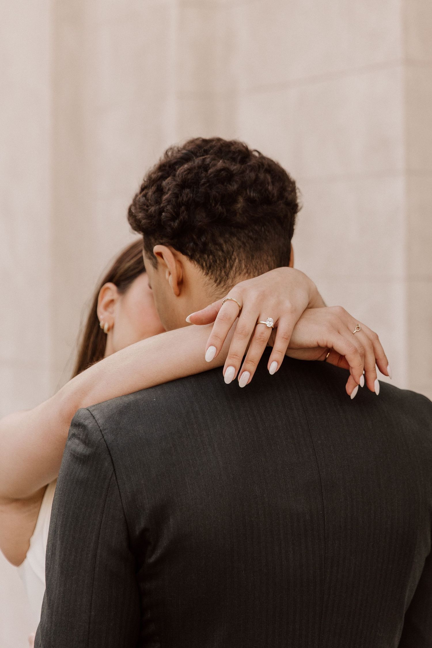 A close up of an couple embracing in a hug. The photo is focusing on her hands that are hanging around his neck
