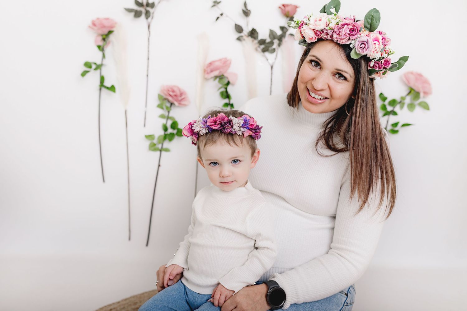 Cheerful family portrait with pink roses and floral crown against white background.