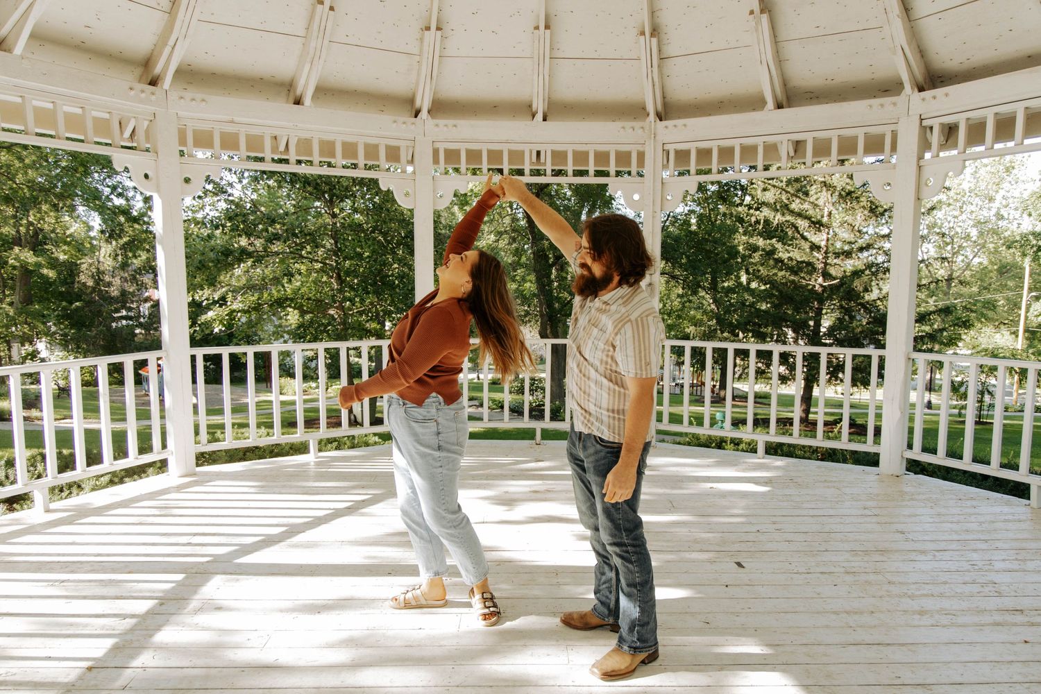 A couple dances together under a white gazebo on a sunny afternoon.