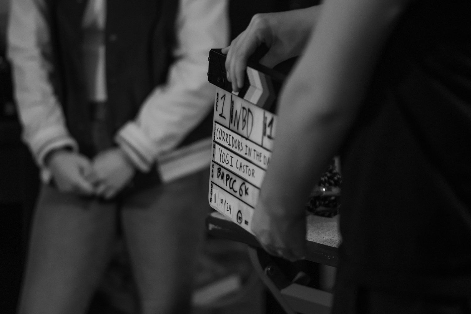 Black and white behind-the-scenes film set photo with a clapperboard being held in front of an actor.