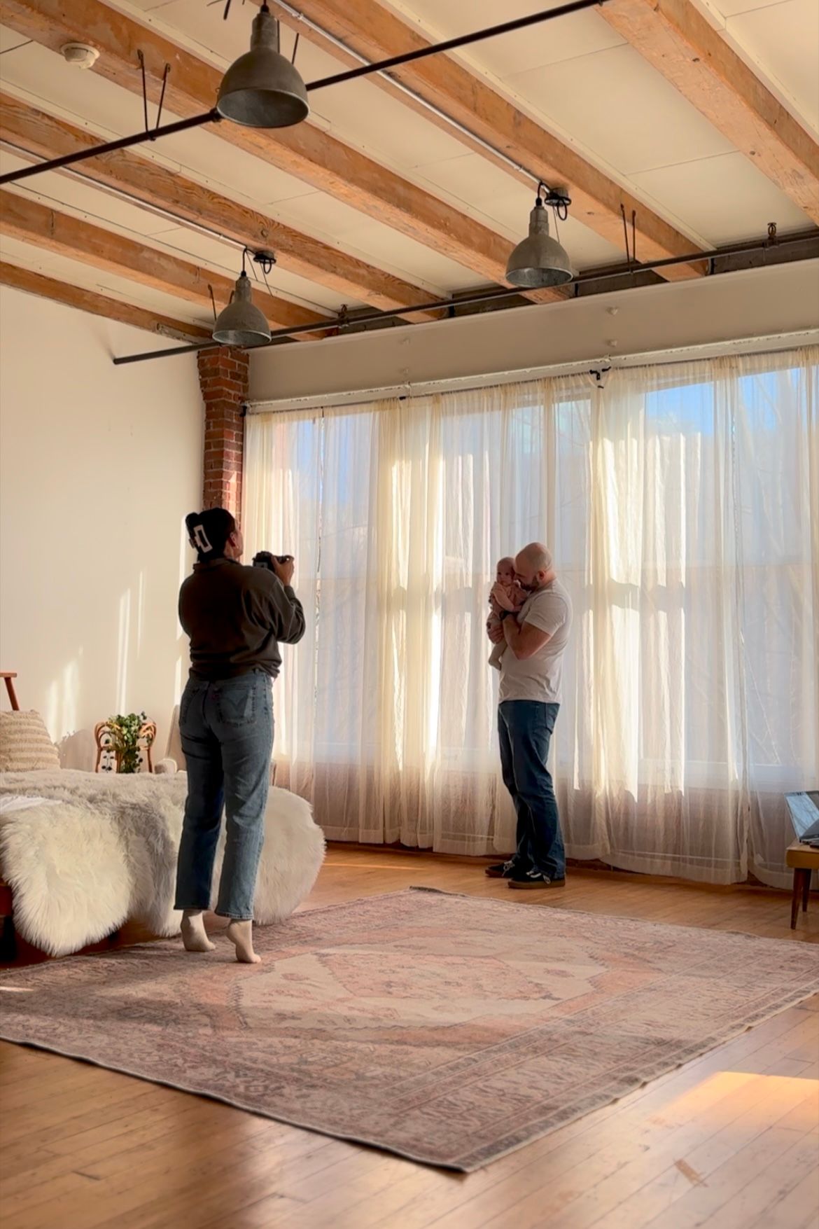 Interior photo of a studio space with exposed wooden beams, industrial lighting and sheer curtains filtering natural light.