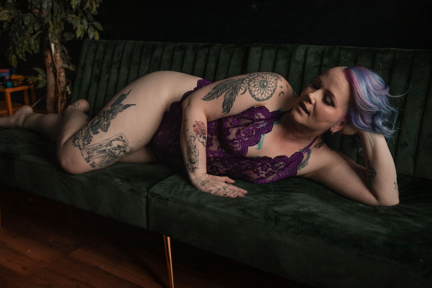 Artistic boudoir photography on a dark couch with moody lighting.