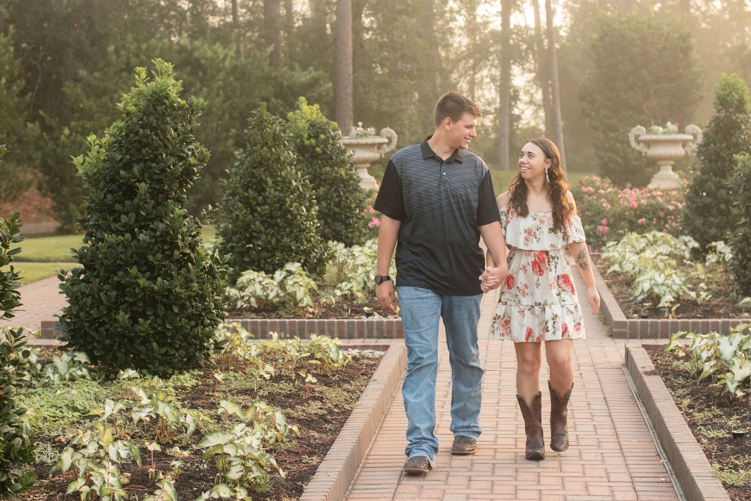 Couple walking together on garden path surrounded by manicured shrubs and flowers.