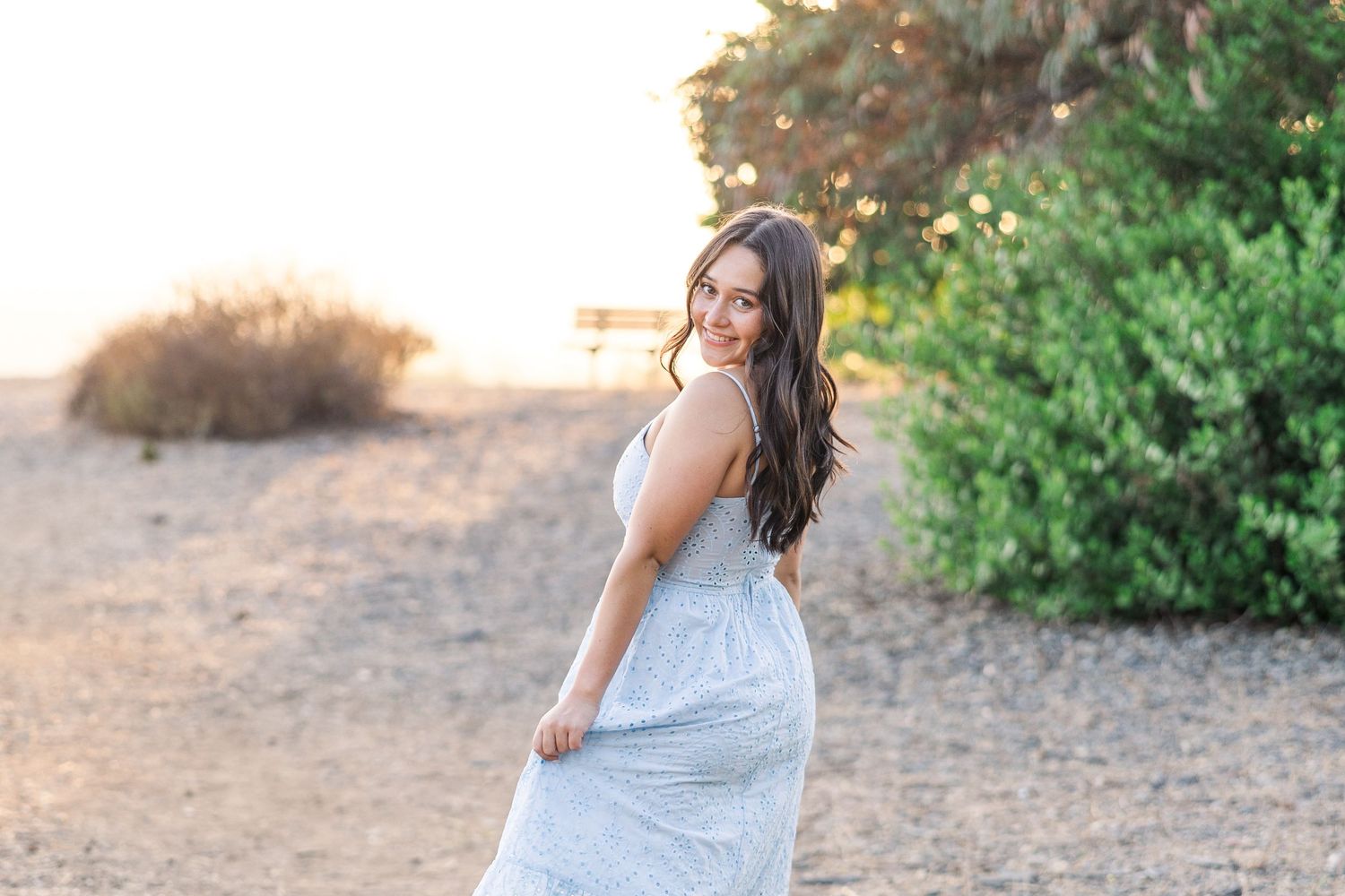 A white summer dress flows gracefully in the sunlight against a natural outdoor backdrop.