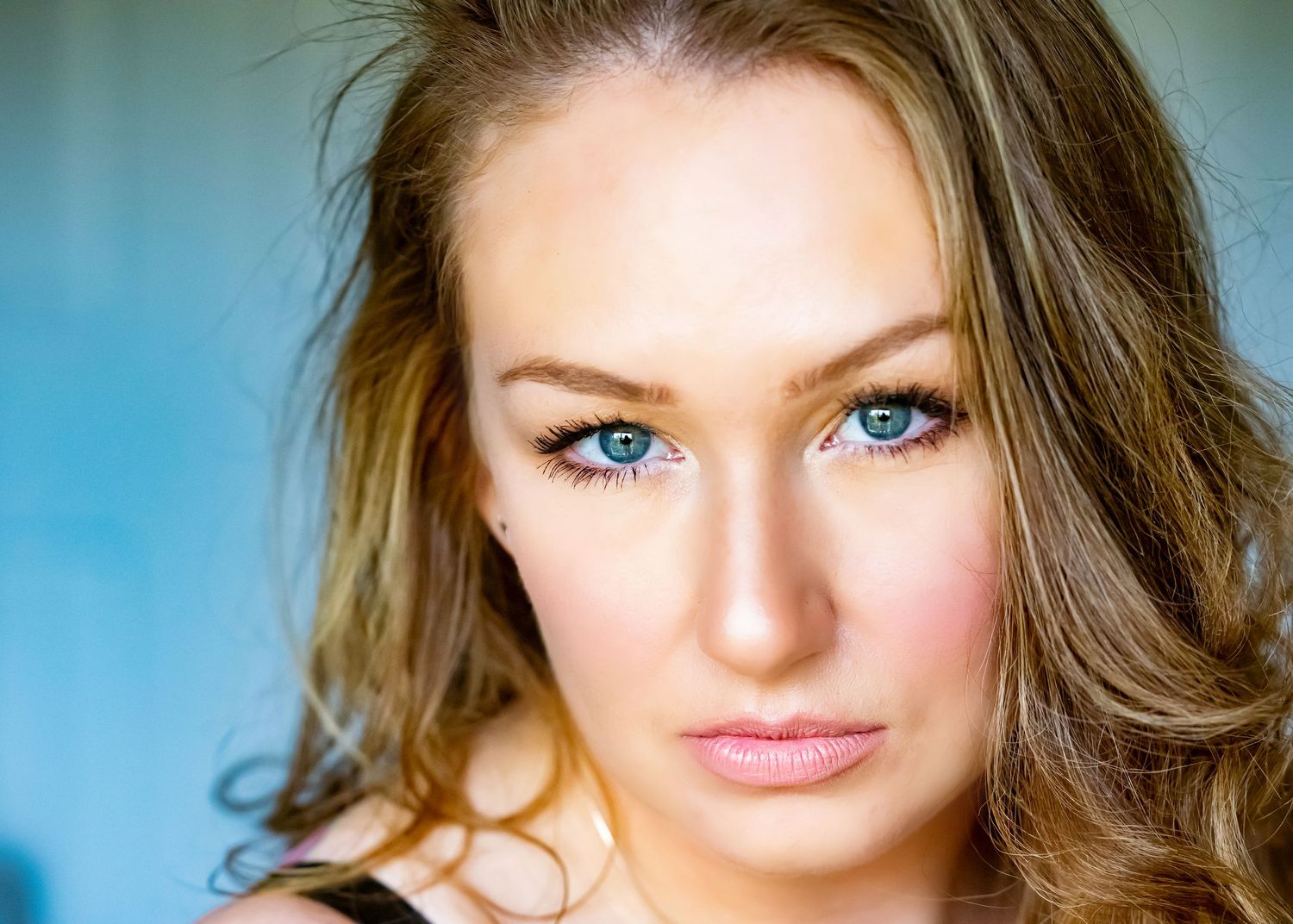 Portrait with bright blue eyes and long wavy brown hair against turquoise background.