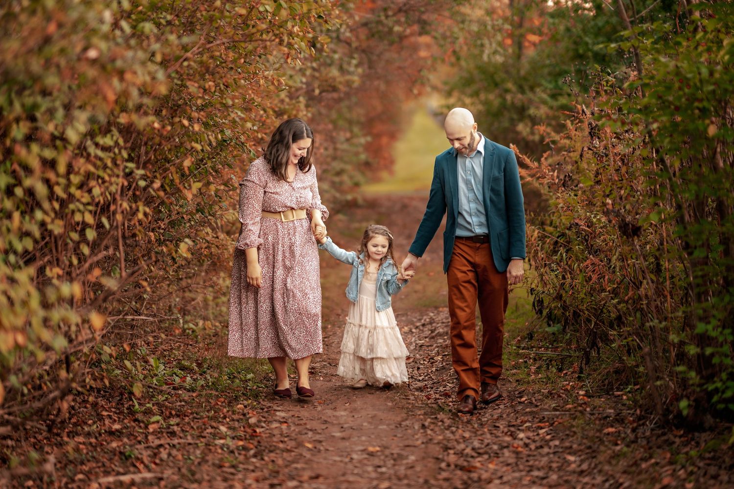 A family walks together on an autumn path surrounded by golden-brown foliage and natural light.