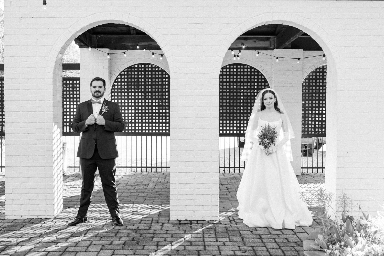 Black and white photo of bride and groom posing separately under arched columns at their outdoor wedding venue.