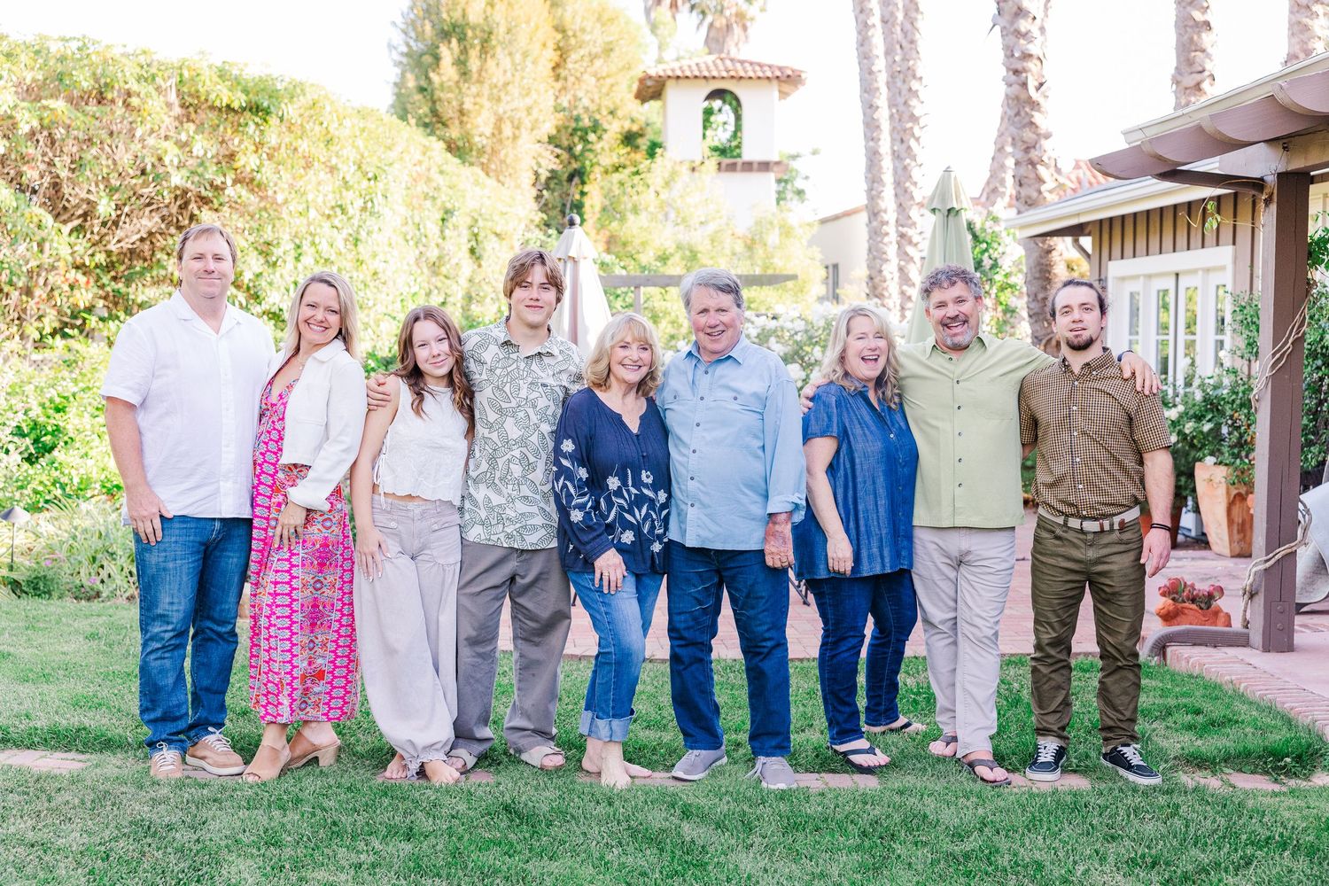 A series of casual outdoor family portraits taken against a wall with palm trees in a garden setting.