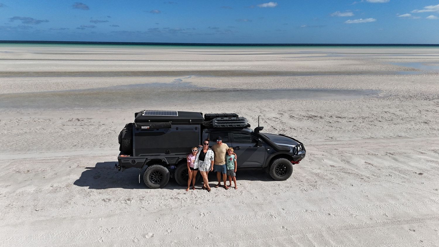 A line of vehicles and people traverse a vast, white salt flat landscape under a bright blue sky.