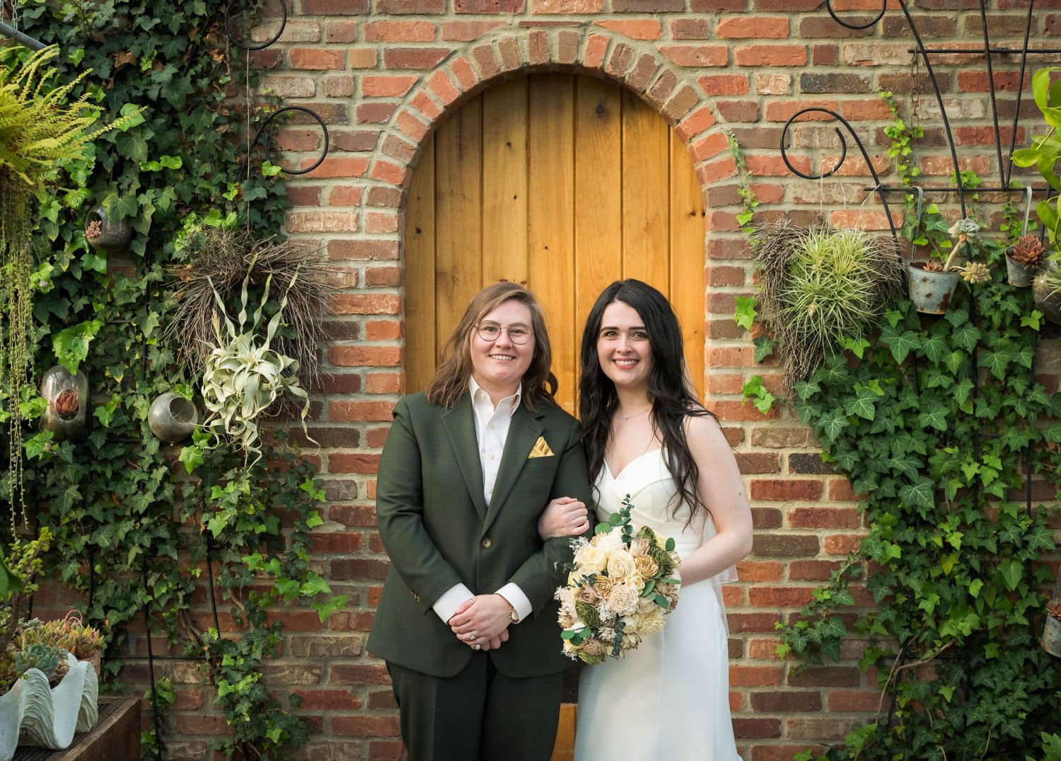 Newlyweds share an intimate moment outdoors with autumn foliage and rustic architecture in background.