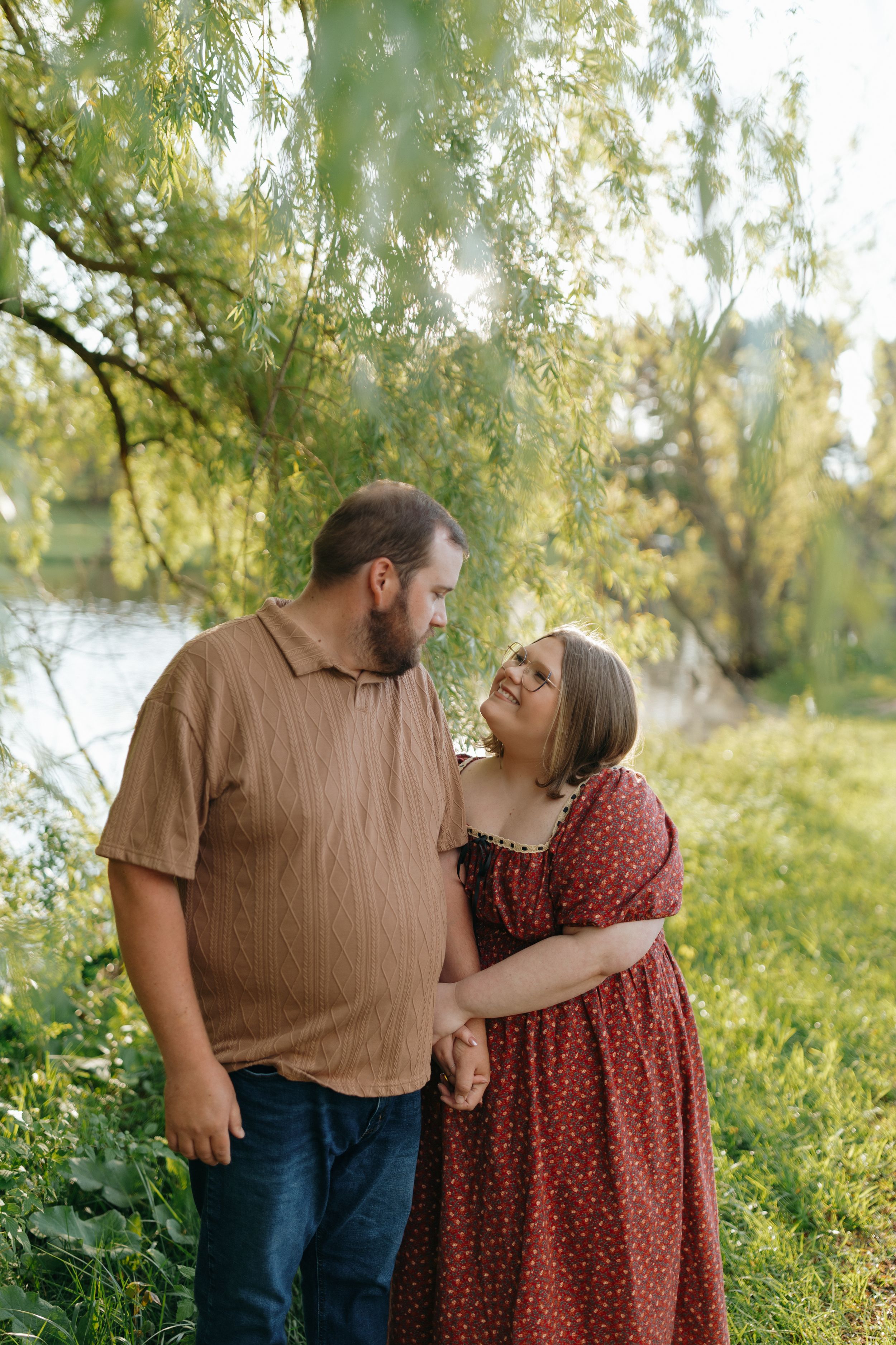 A couple shares tender moments outdoors under willow trees in a romantic autumn photoshoot.