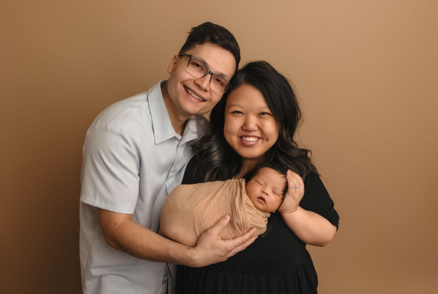 Beautiful couple dressed in natural colors lovingly hold their sleeping newborn at Charlottesville photography studio.