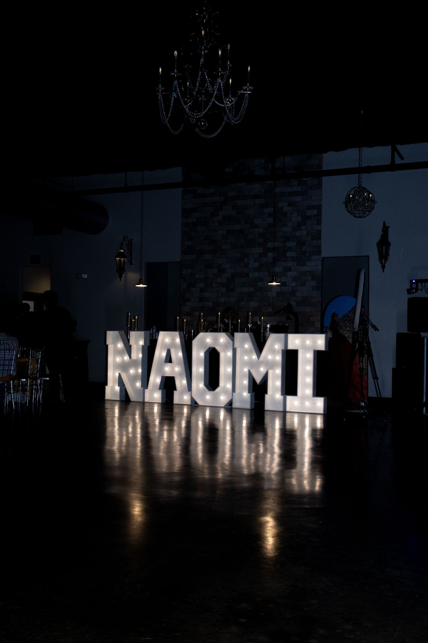 Illuminated white letters spelling out NAOMT on a dark wall create a glowing display in a dimly lit space.