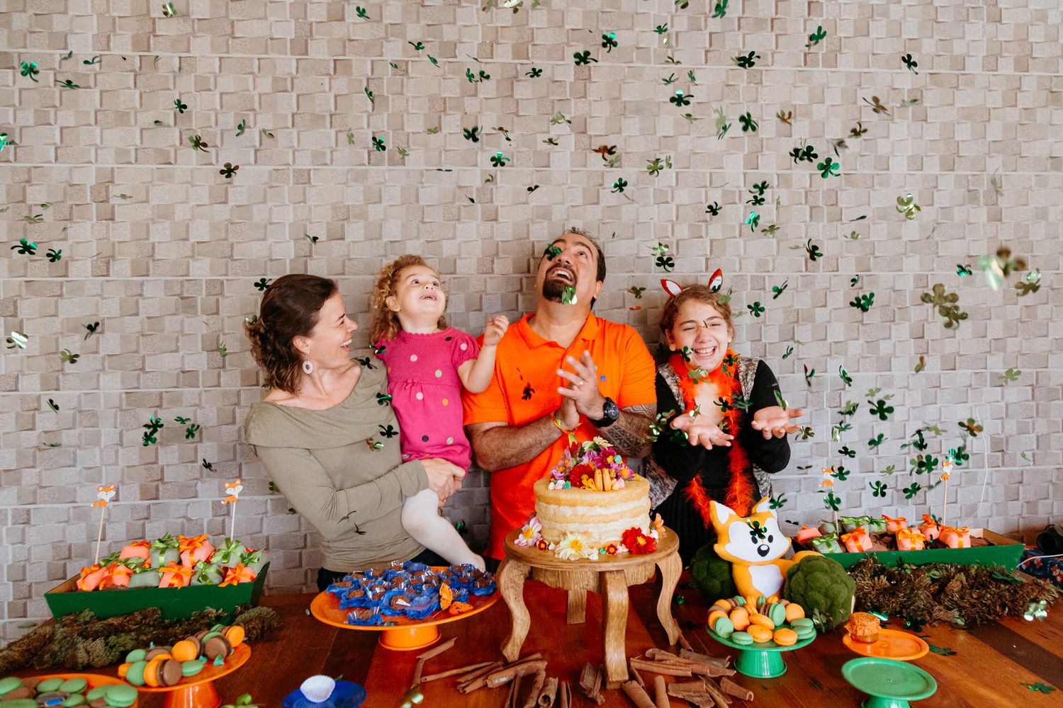 Joyful group celebrates at a festive party with confetti falling and colorful food displays on wooden table.