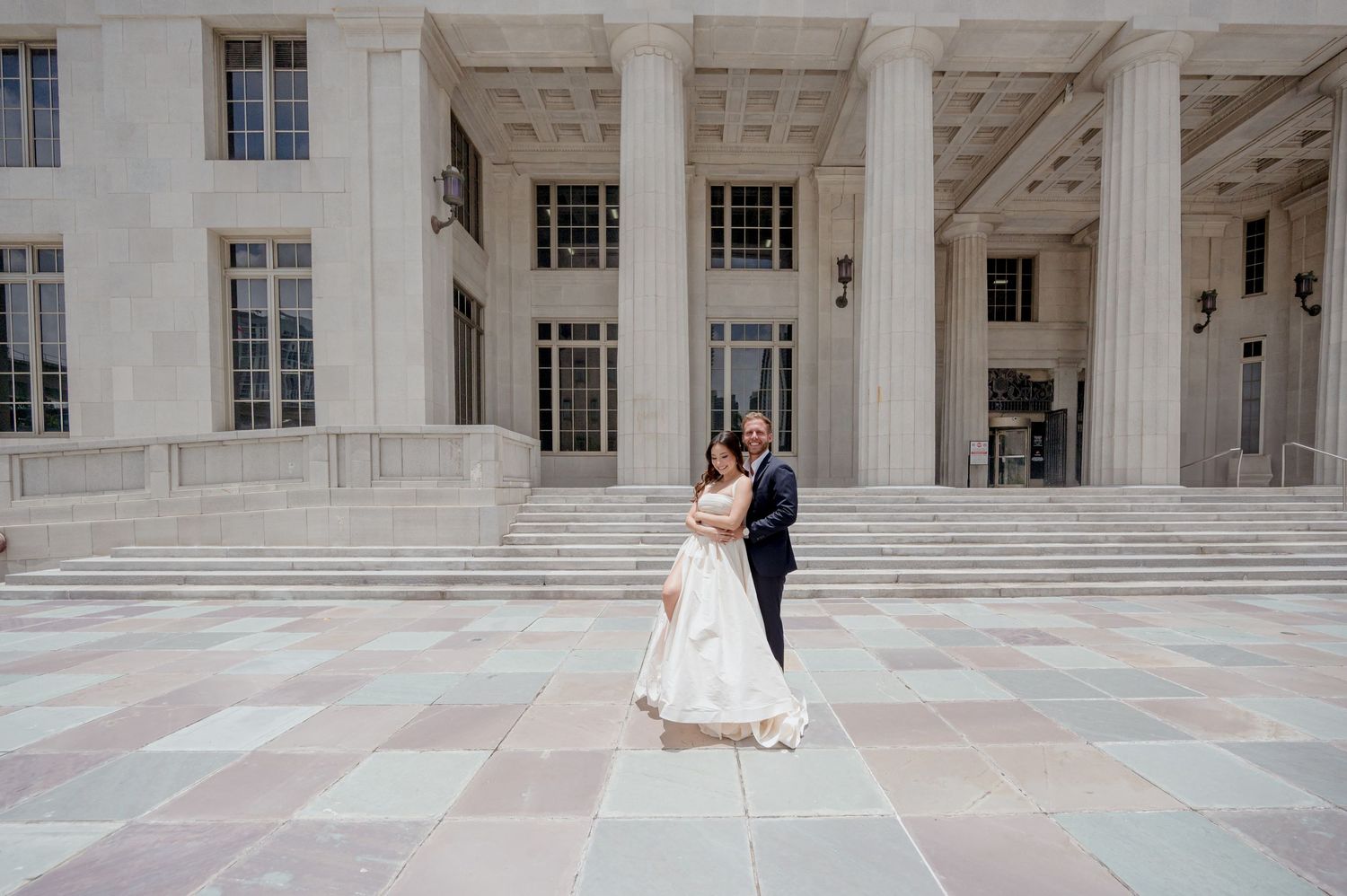 A couple poses on a grand marble staircase in front of a neoclassical building with tall white columns.