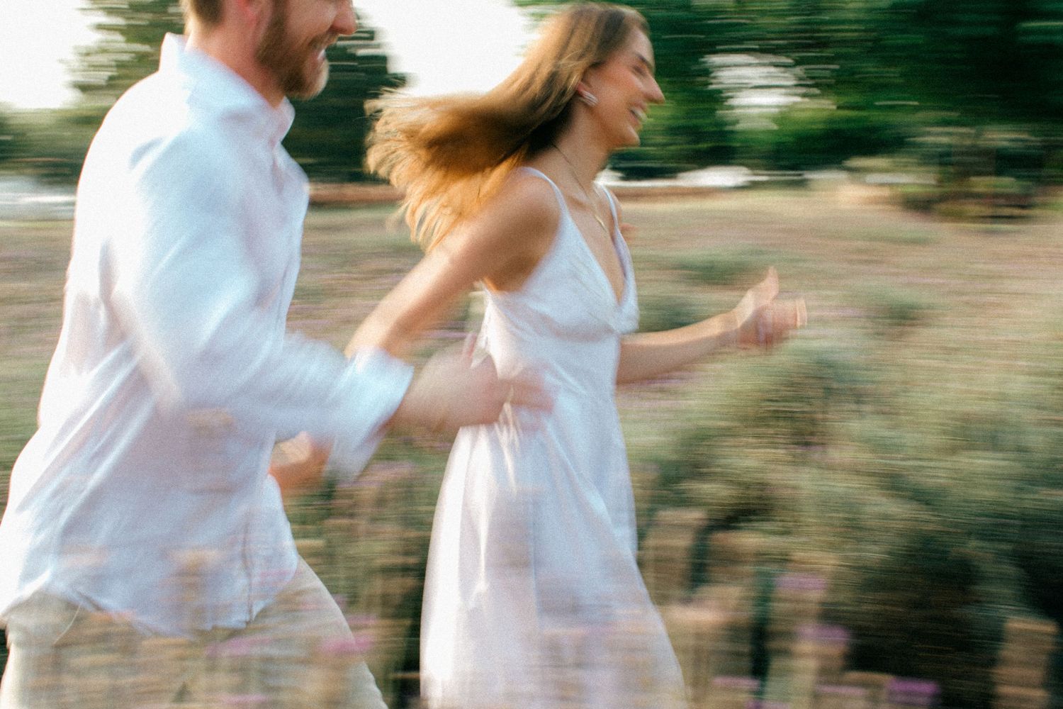 Motion blur photo of couple in white clothing running together outdoors in natural setting.