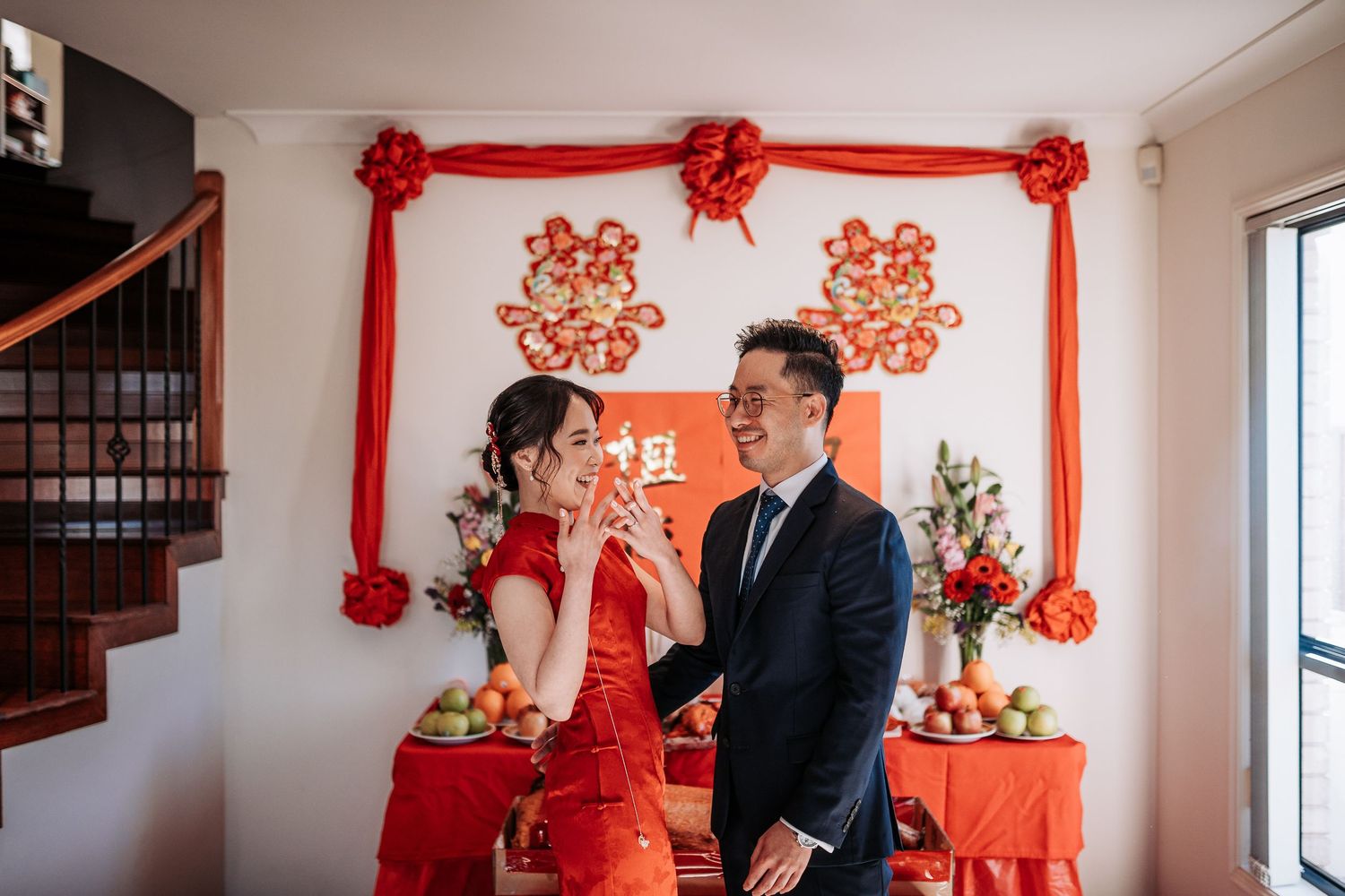 Traditional Chinese wedding ceremony with couple in formal attire standing in front of red decorations and altar.