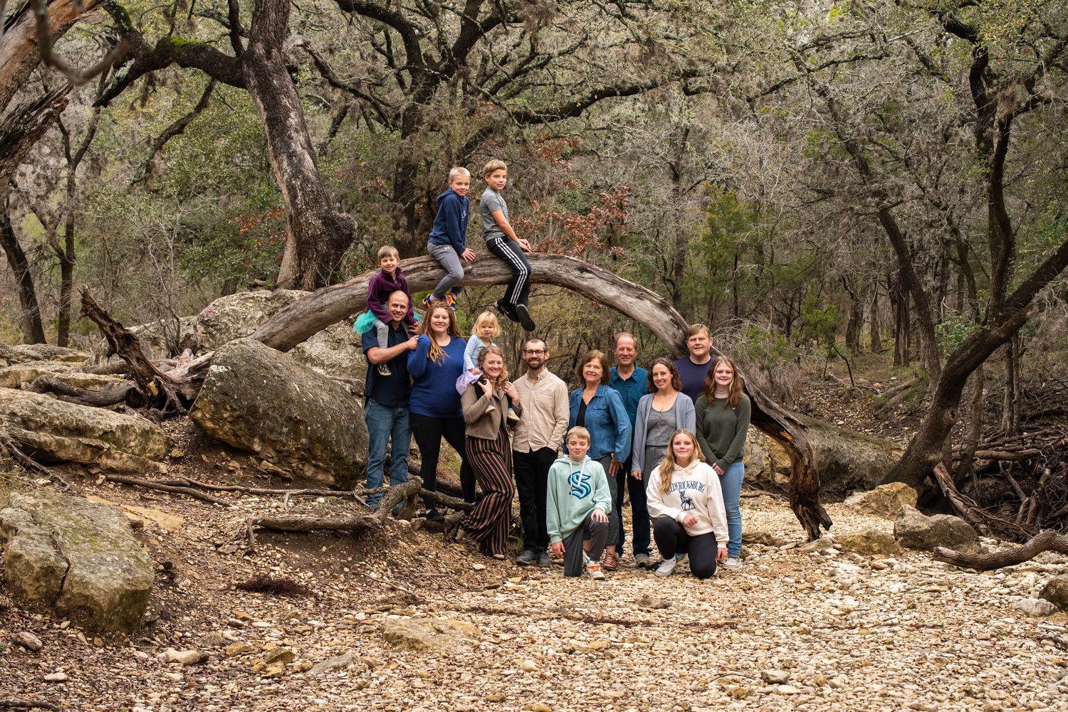 A group of people stand together under shaded trees in an outdoor natural setting in warm sunlight.