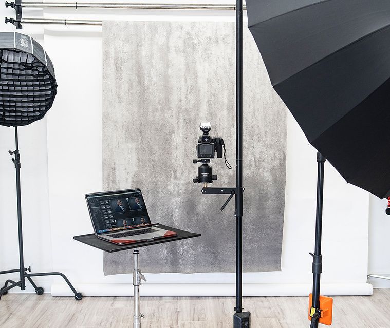 Photography studio setup with lighting equipment, laptop and umbrella against concrete wall.