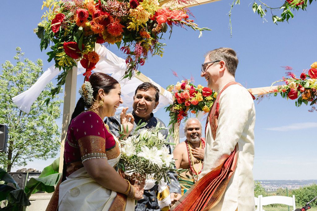 A vibrant outdoor Indian wedding ceremony under blue skies with floral decorations and traditional attire.