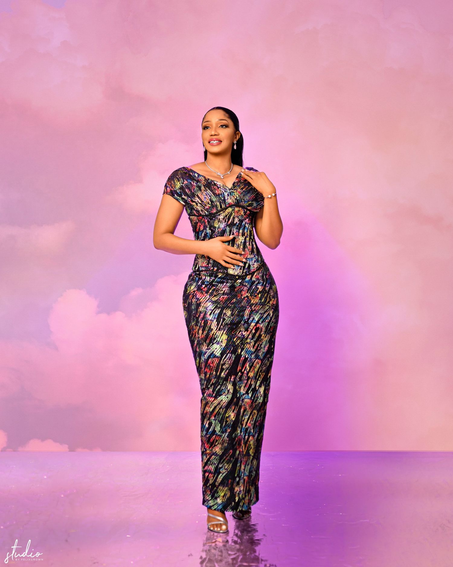 Woman models a sparkling pink sequined evening gown in a studio setting.