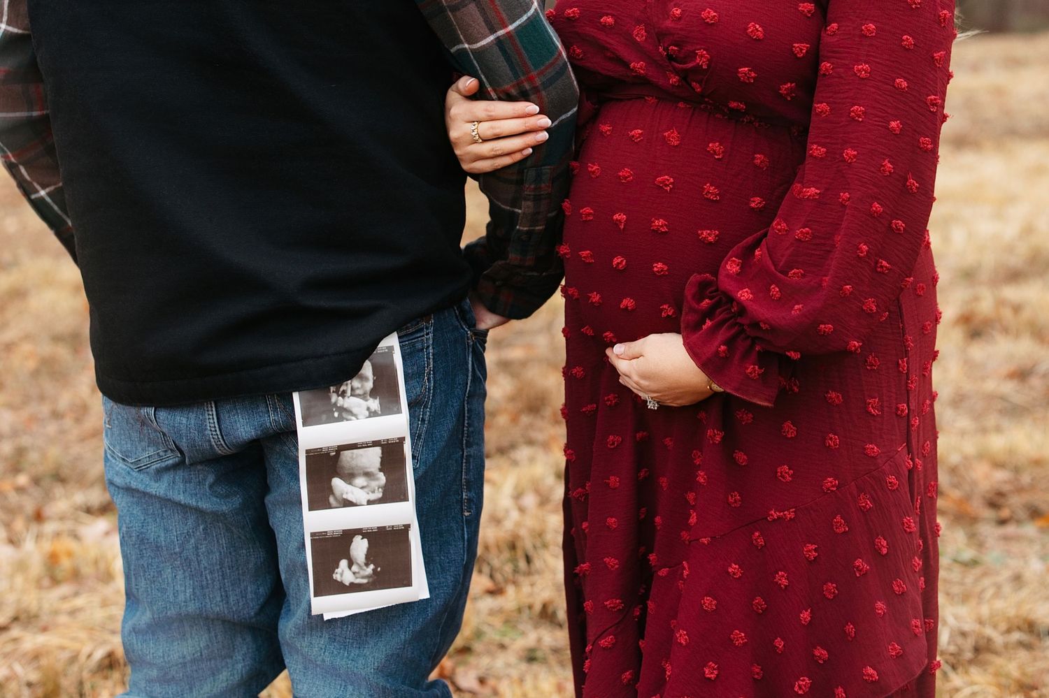 Couple holding ultrasound photos with person wearing red polka dot dress and jeans in autumn setting.