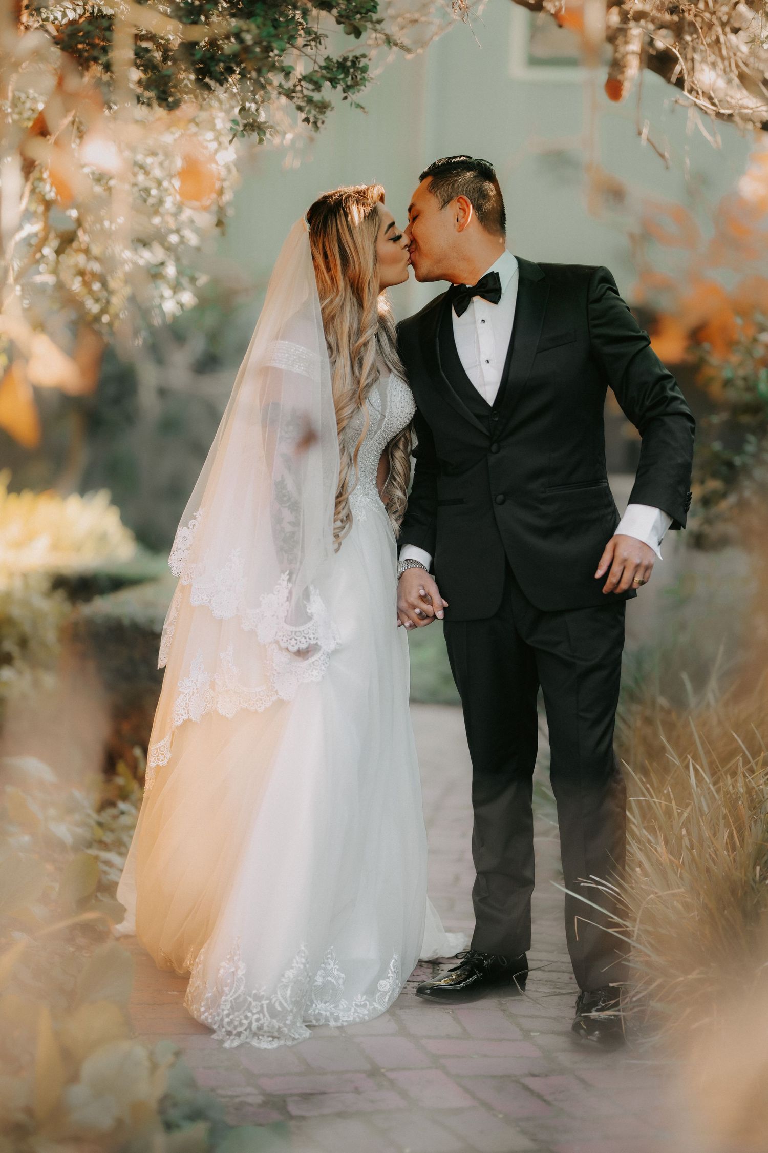 A romantic wedding couple walks together on a path surrounded by autumn foliage and soft lighting.
