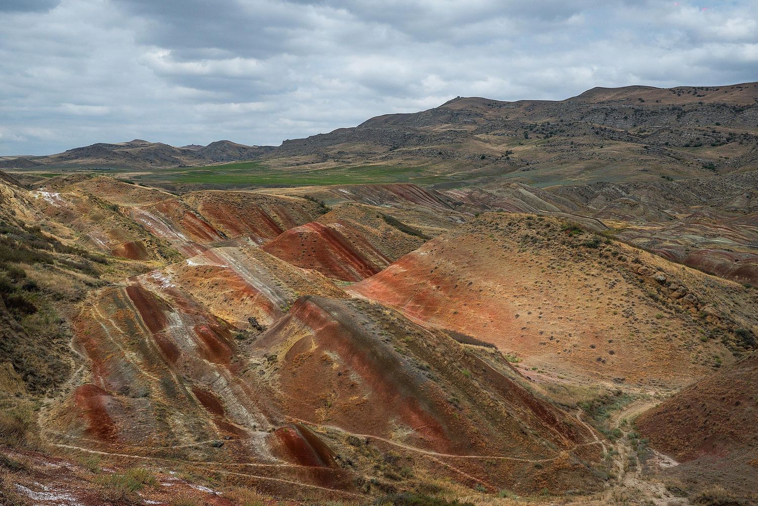Panoramic view of colorful layered mountains with red and brown striped rock formations under cloudy skies.