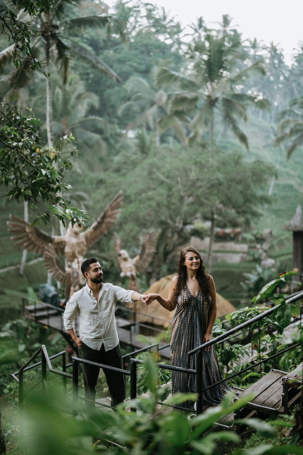 A couple poses on a rope bridge surrounded by tropical vegetation.