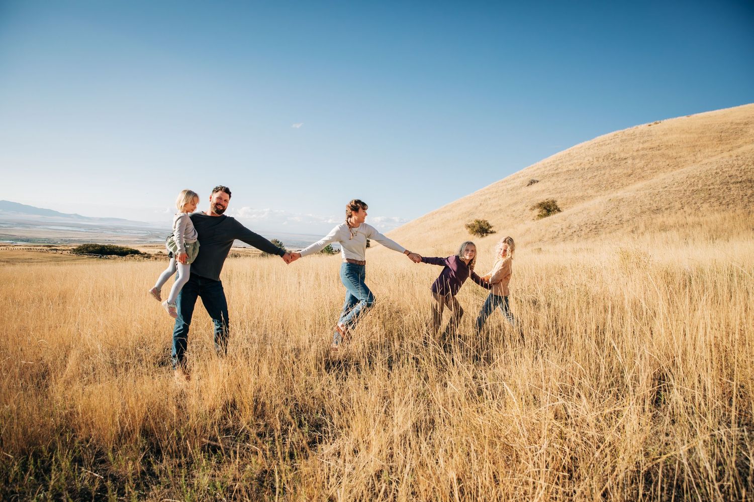 People holding hands and running through a golden wheat field at sunset.