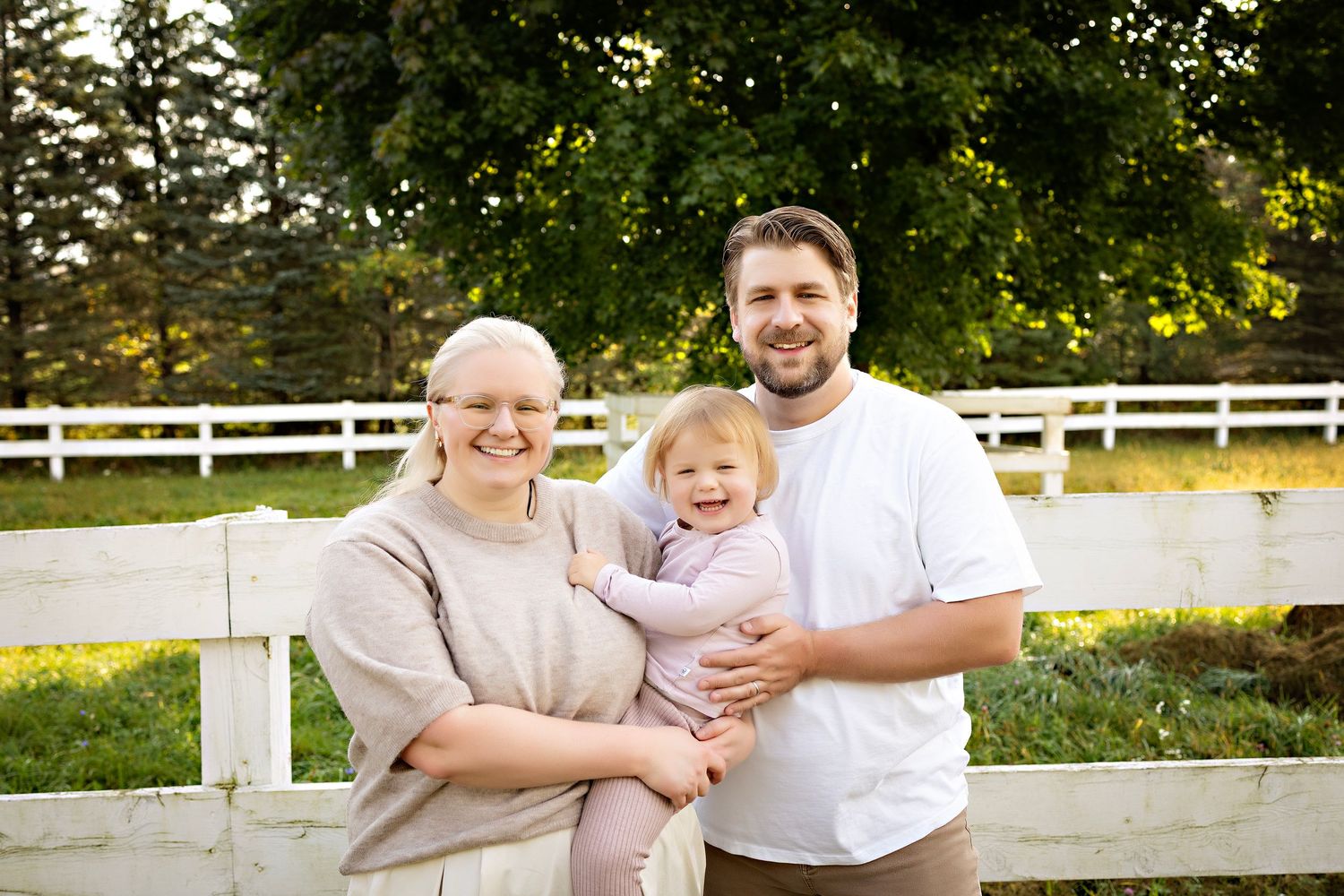 Family enjoying a sunny day together outdoors near a white fence in a park setting.