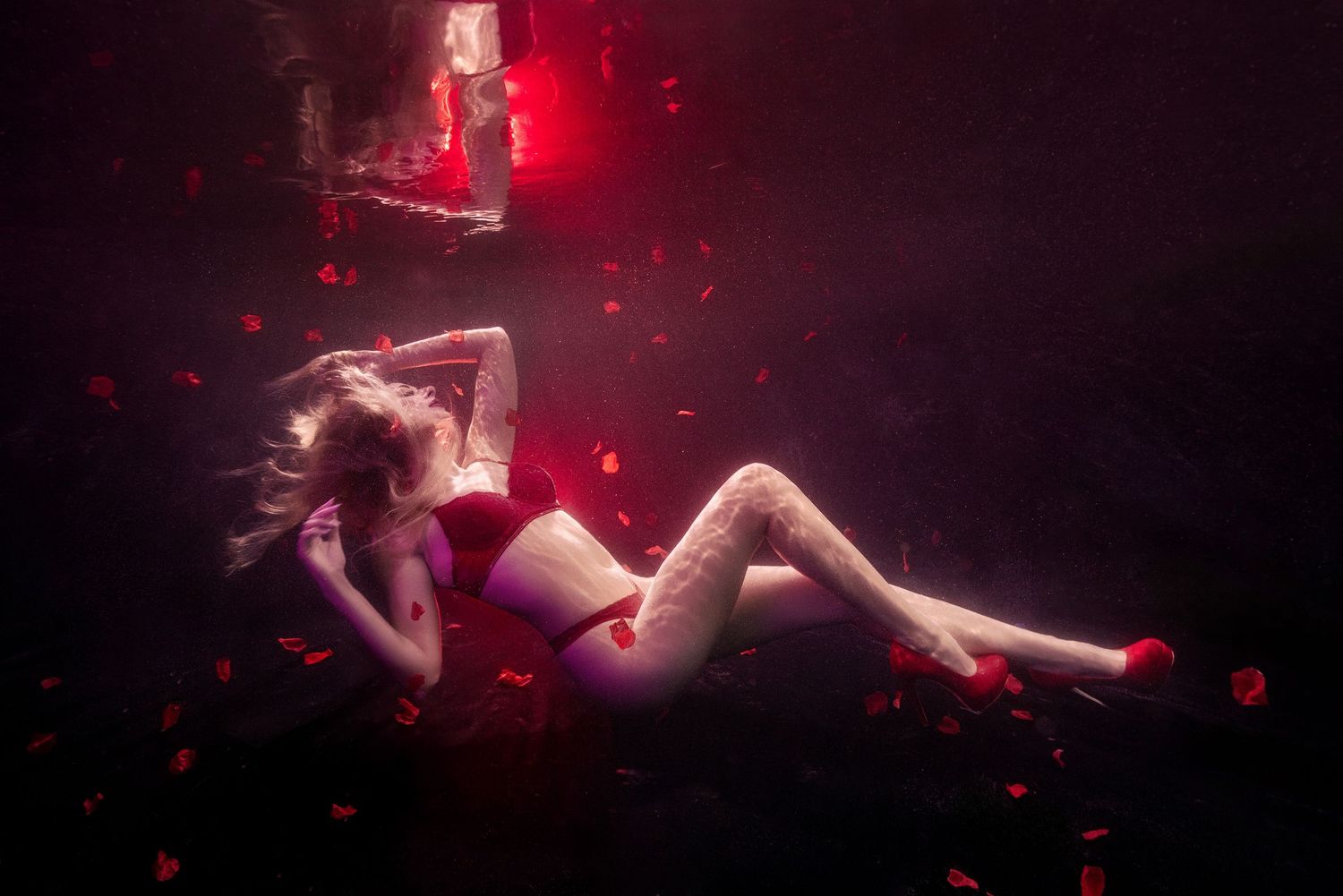 Underwater fashion photo with flowing red dress and nurse sharks swimming in crystal clear turquoise waters.