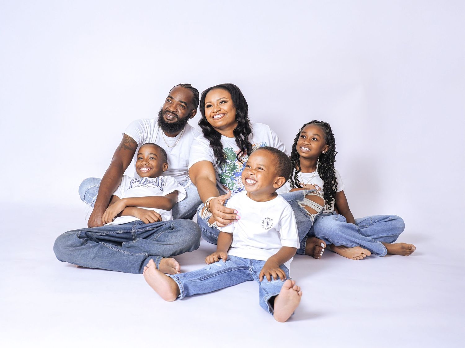 Happy family of five posing together in white outfits and jeans against a white studio background.