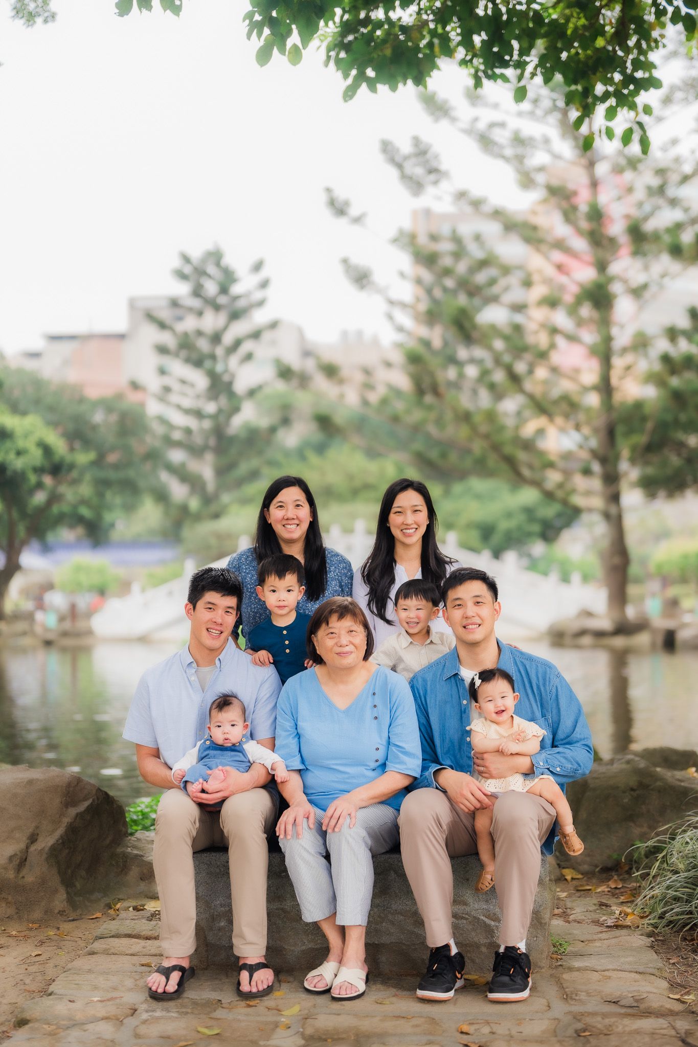 A family sits together on a stone ledge by a lake with trees in the background.