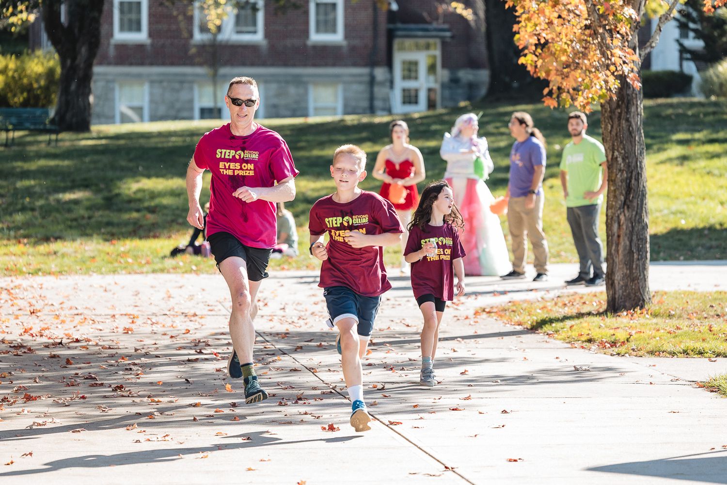 A group of runners jogs along a tree-lined path during a sunny autumn day.