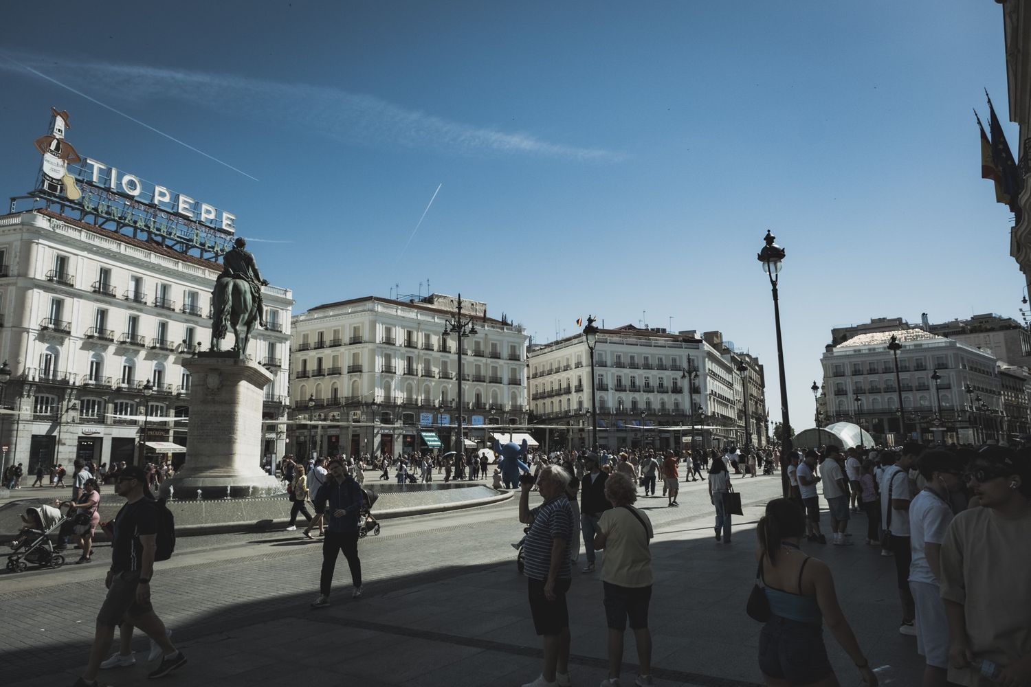 Busy Puerta del Sol plaza in Madrid featuring Tio Pepe billboard, classical architecture, and crowds under blue sky.