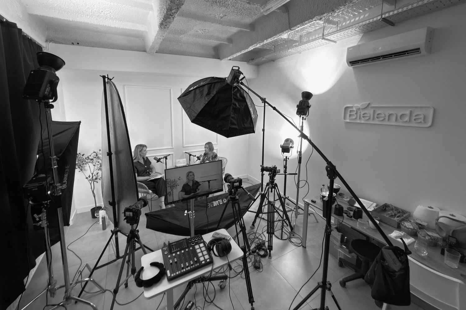 Black and white photo of a professional photography studio with softbox lights, stands, and two people being photographed.