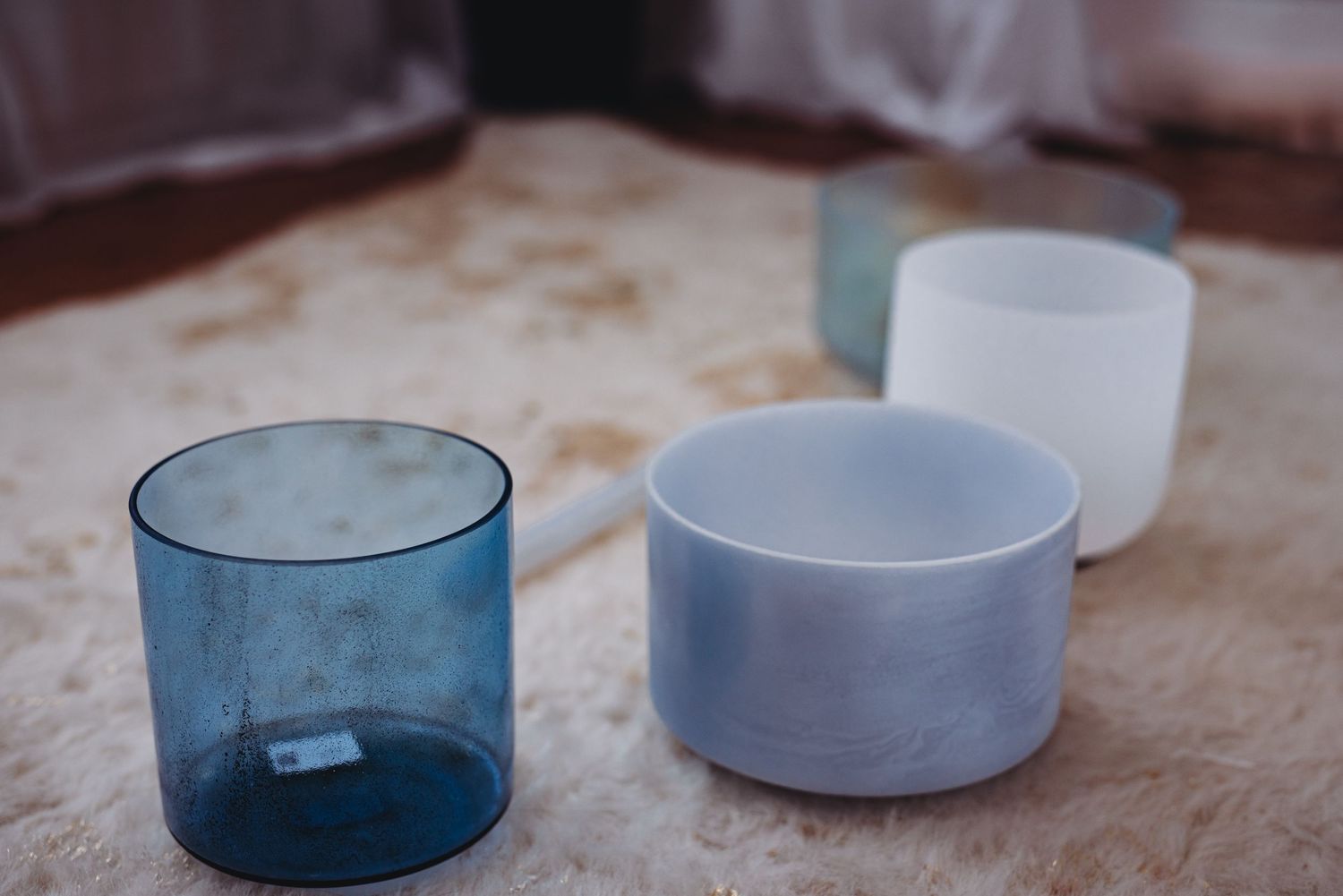 Translucent blue and frosted white crystal singing bowls resting on a soft white surface.