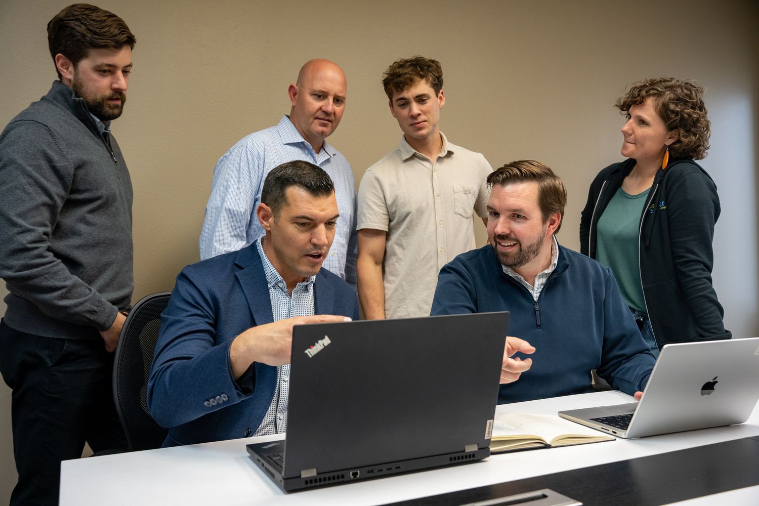 Business professionals collaborate around laptops during a team meeting in a modern office setting.