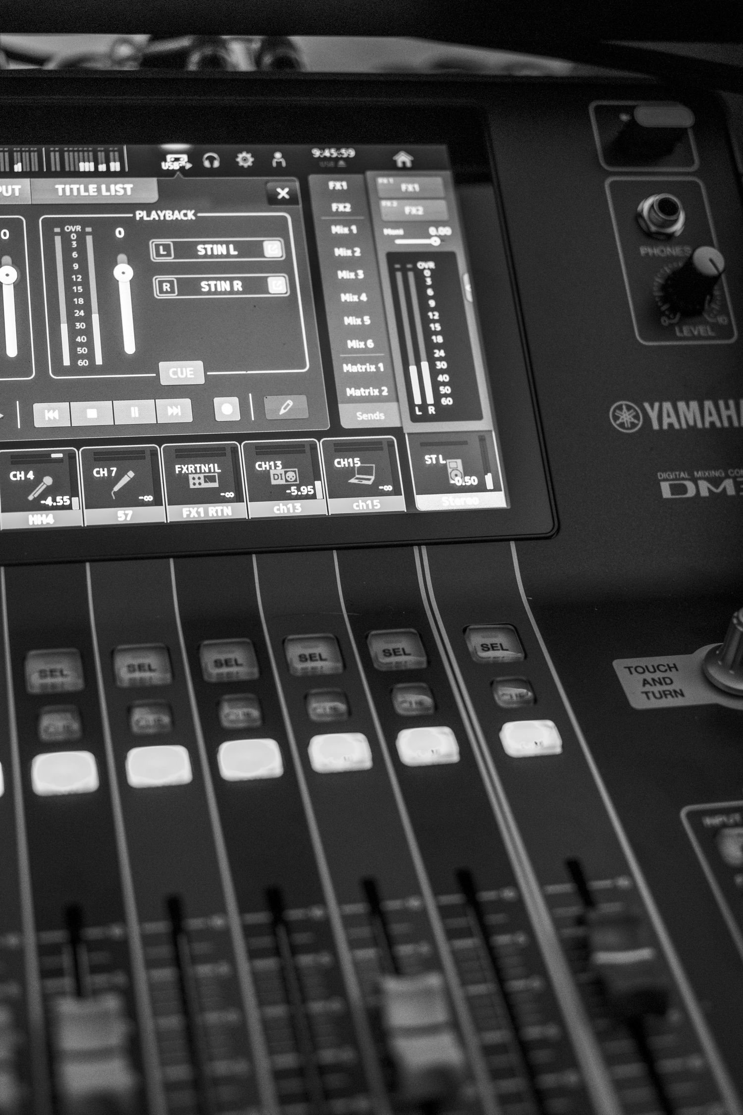 Black and white close-up of a Yamaha DM digital audio mixing console with faders and touchscreen display.