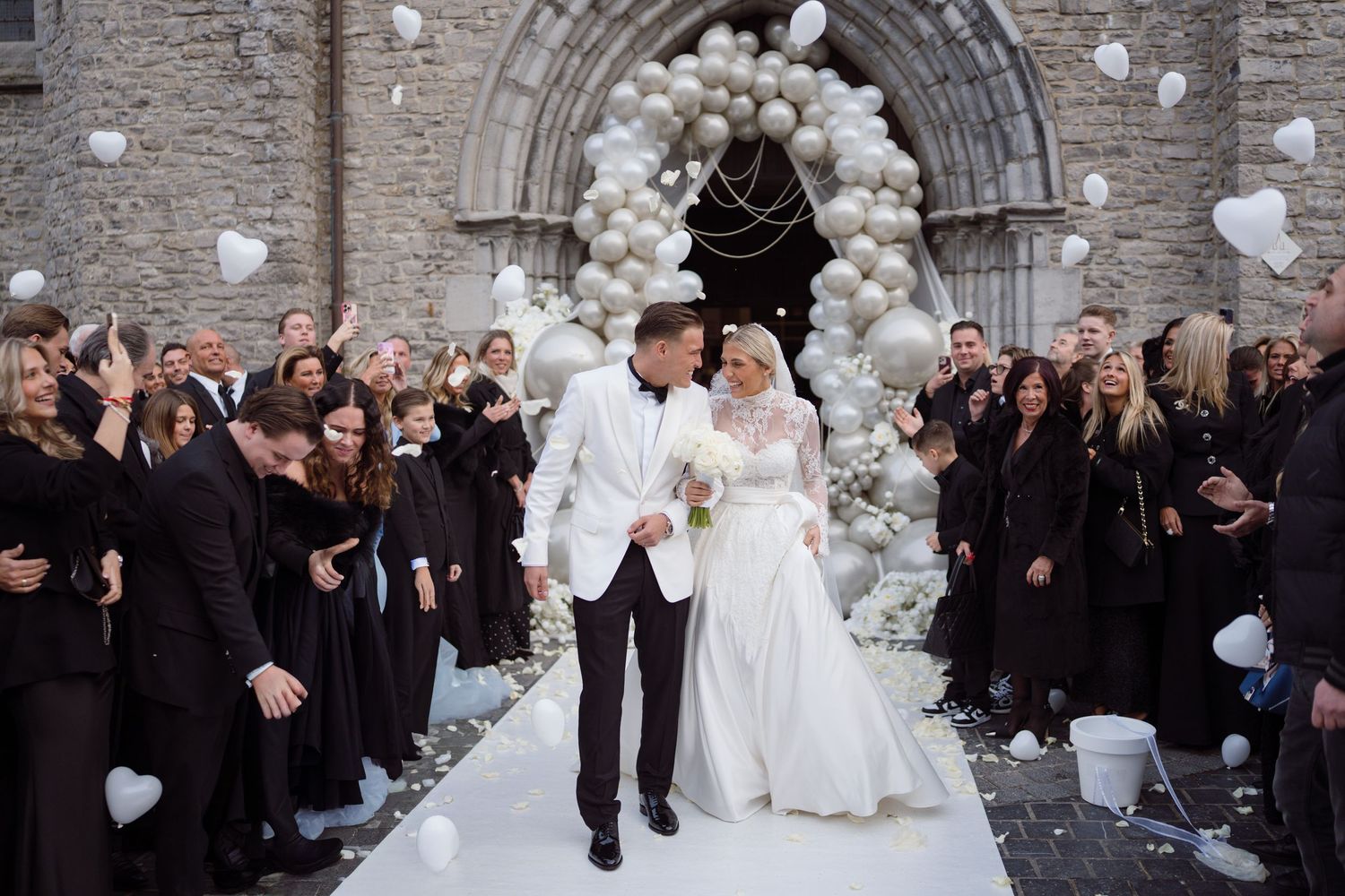 Wedding guests release white balloons outside a stone church during a celebration ceremony.