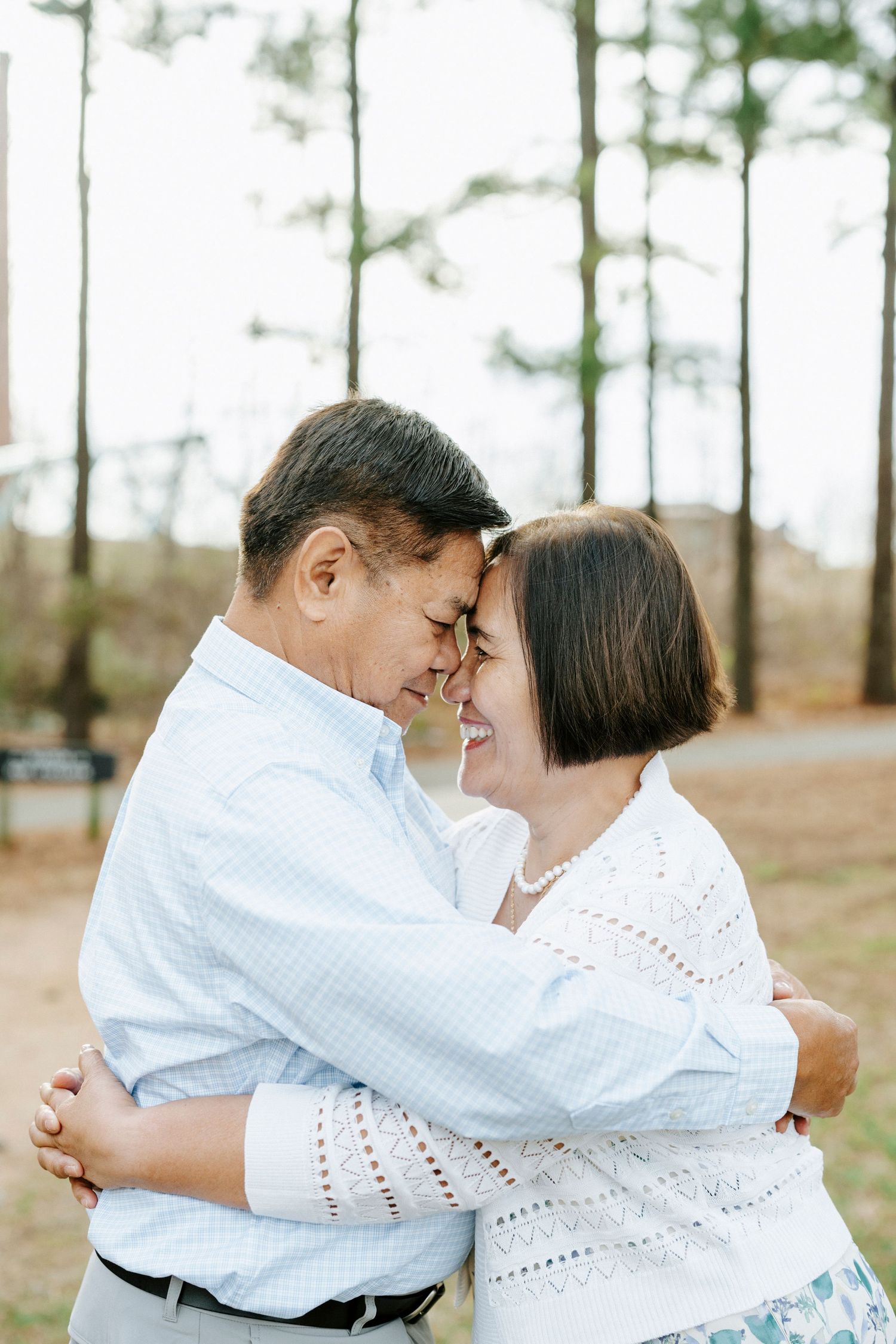 Romantic couple in white outfits share tender moments together in a pine forest setting.