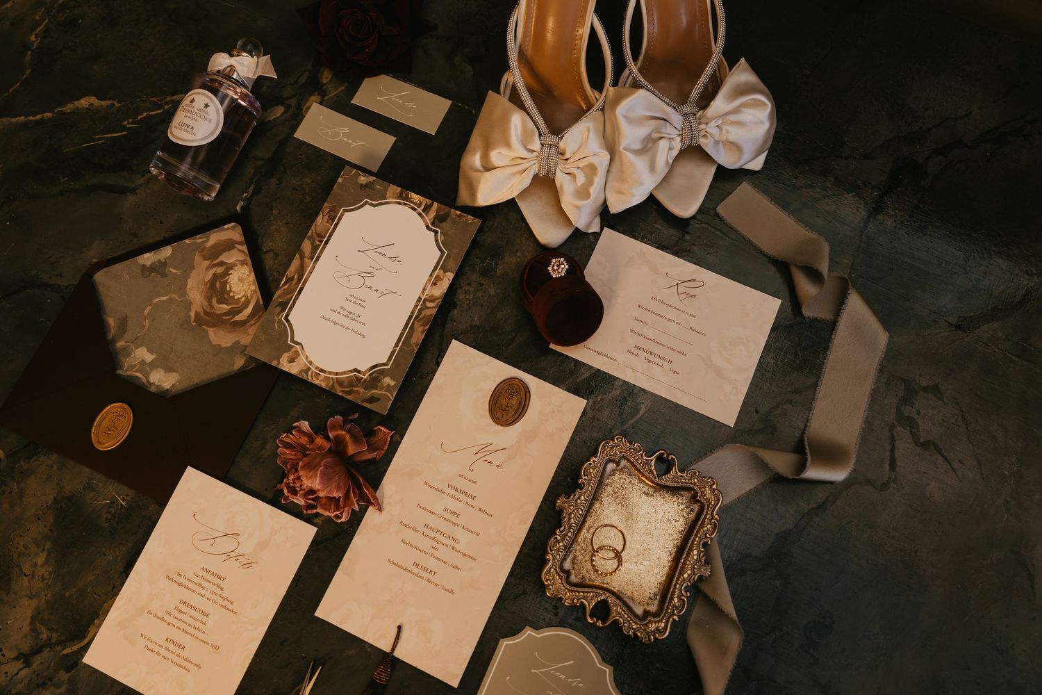 Wedding invitation suite with elegant calligraphy, floral details and wax seals arranged on dark moody background.