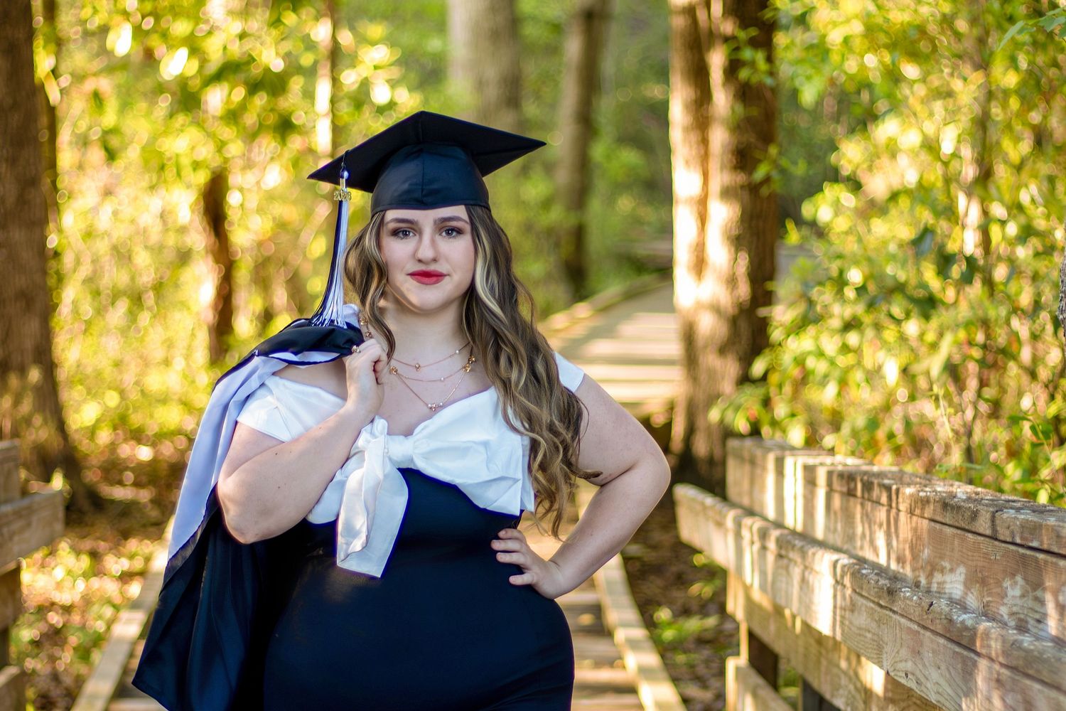 Young woman in graduation cap and gown posing in trees. family photography, senior photos, graduate sessions, portraits, wedding photography